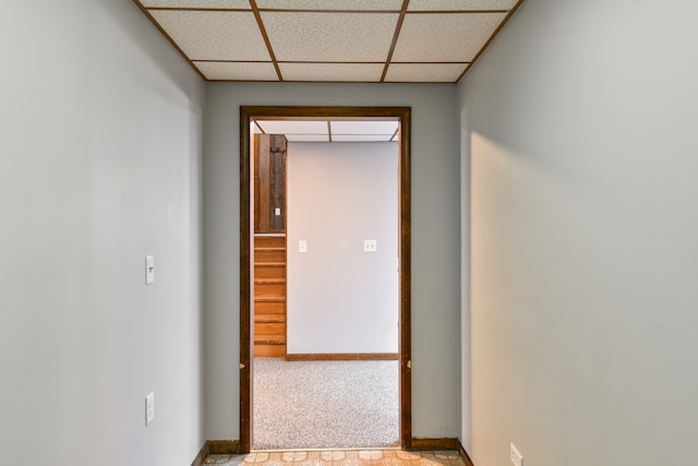 hallway featuring a paneled ceiling, baseboards, and light colored carpet