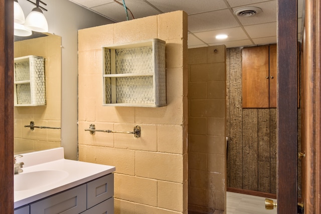 bathroom with concrete block wall, visible vents, a paneled ceiling, and vanity