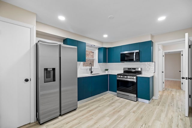 kitchen with appliances with stainless steel finishes, blue cabinetry, sink, and light hardwood / wood-style floors