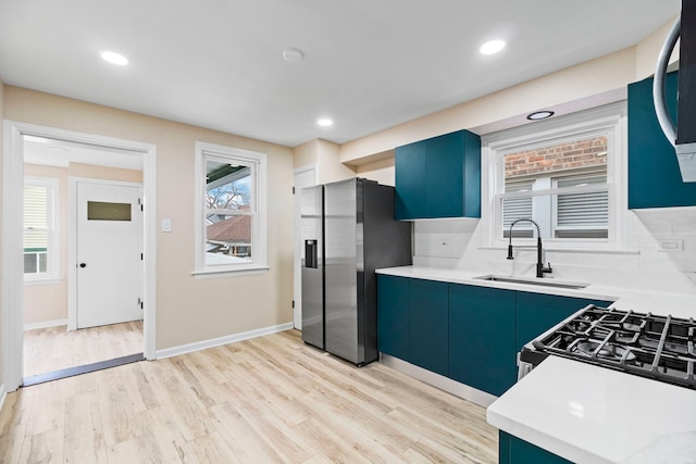 kitchen featuring blue cabinetry, sink, appliances with stainless steel finishes, light hardwood / wood-style floors, and backsplash