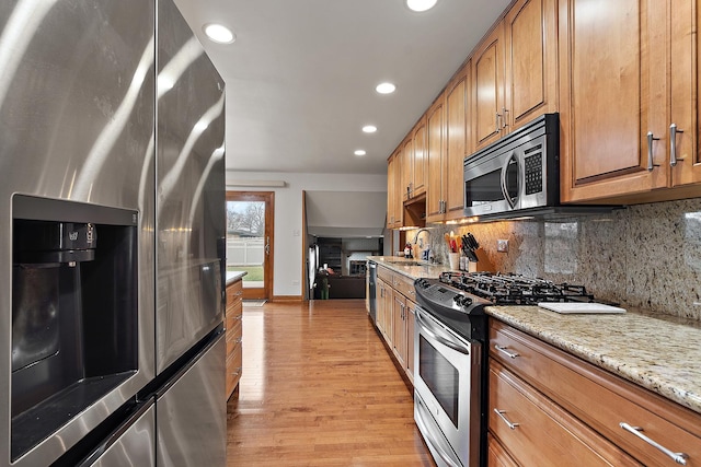 kitchen featuring appliances with stainless steel finishes, sink, decorative backsplash, light hardwood / wood-style floors, and light stone countertops