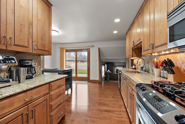 kitchen with sink, appliances with stainless steel finishes, light stone counters, tasteful backsplash, and light wood-type flooring