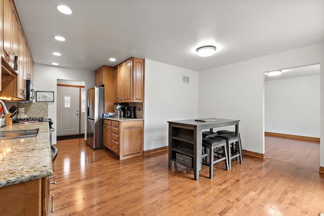 kitchen with light stone countertops, decorative backsplash, stainless steel appliances, and light hardwood / wood-style floors