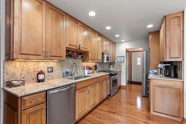 kitchen with sink, tasteful backsplash, light wood-type flooring, appliances with stainless steel finishes, and light stone countertops