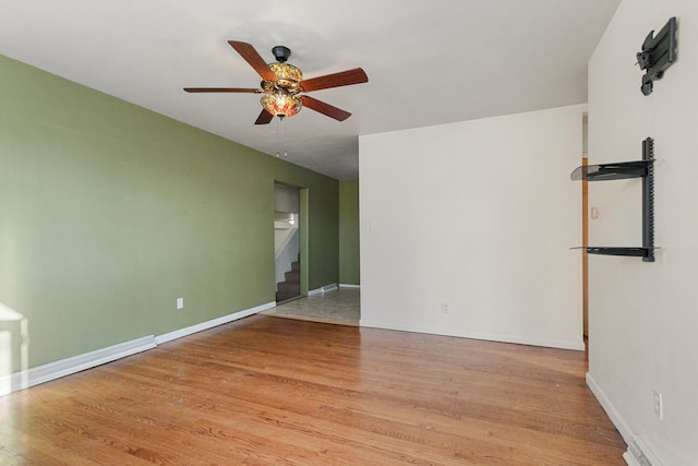 empty room featuring stairs, baseboards, light wood-type flooring, and a ceiling fan