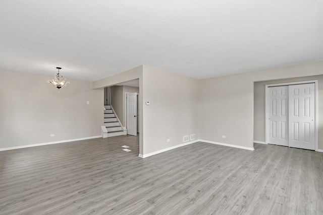 unfurnished living room featuring light wood-style floors, baseboards, stairway, and an inviting chandelier