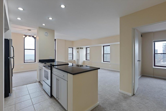 kitchen featuring range with electric stovetop, white cabinetry, stainless steel fridge, light colored carpet, and a healthy amount of sunlight