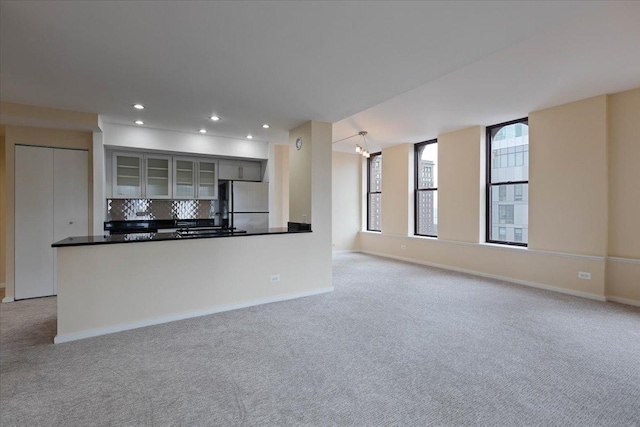 kitchen featuring stainless steel refrigerator, light colored carpet, kitchen peninsula, and decorative backsplash