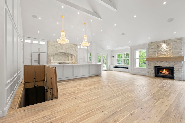 kitchen with a large island, high vaulted ceiling, a fireplace, white cabinets, and decorative light fixtures