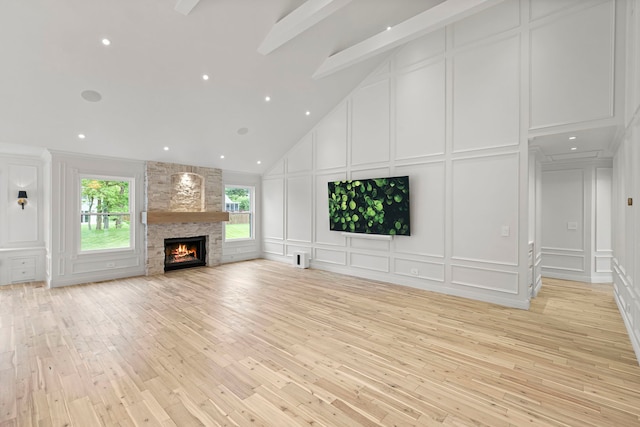 unfurnished living room featuring beam ceiling, high vaulted ceiling, a fireplace, and light hardwood / wood-style flooring