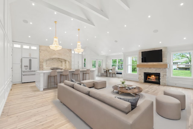 living room with beamed ceiling, a large fireplace, light hardwood / wood-style floors, and a wealth of natural light