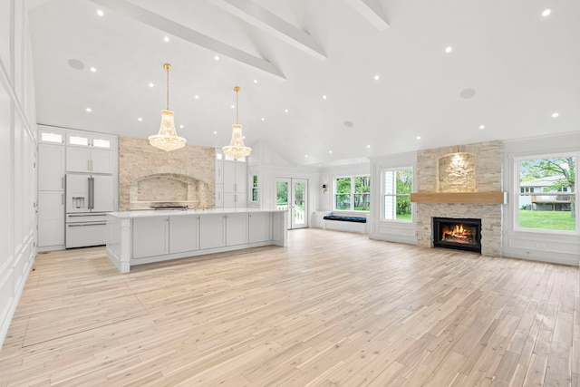 kitchen featuring a spacious island, a stone fireplace, built in fridge, pendant lighting, and white cabinets