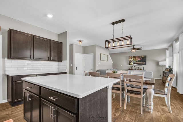 kitchen with decorative light fixtures, dark brown cabinets, dark hardwood / wood-style floors, a kitchen island, and decorative backsplash