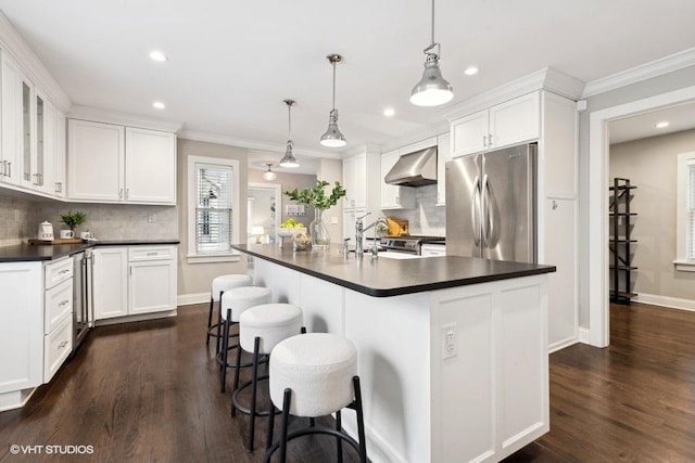 kitchen featuring wall chimney exhaust hood, a center island with sink, stainless steel fridge, pendant lighting, and white cabinets