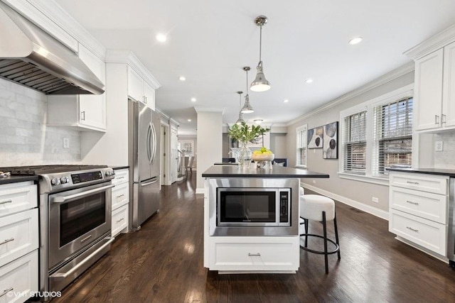 kitchen with appliances with stainless steel finishes, decorative light fixtures, range hood, white cabinets, and backsplash