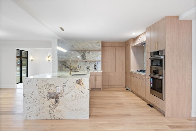 kitchen with double oven, light brown cabinetry, decorative light fixtures, sink, and light stone countertops