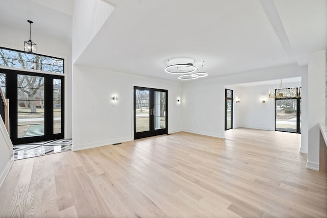 unfurnished living room featuring light hardwood / wood-style floors, an inviting chandelier, and french doors