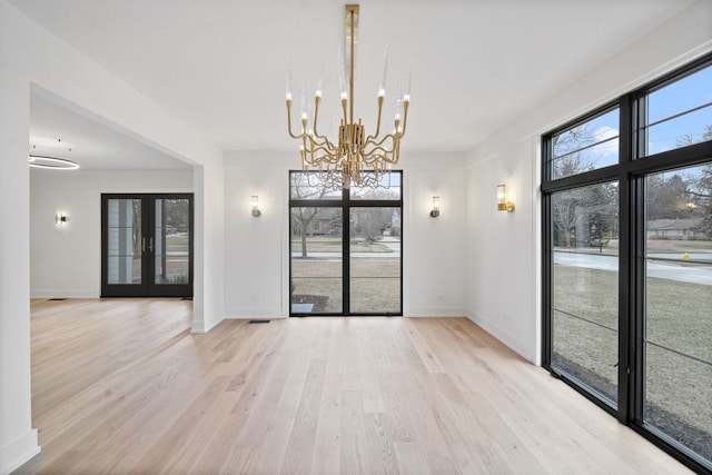 unfurnished dining area with a notable chandelier, french doors, and light wood-type flooring