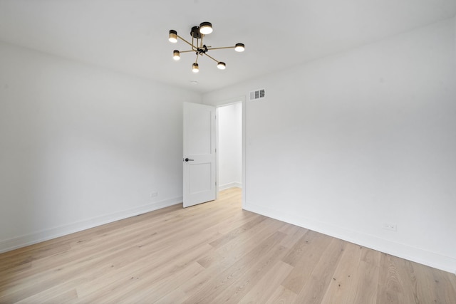 empty room featuring an inviting chandelier and light wood-type flooring