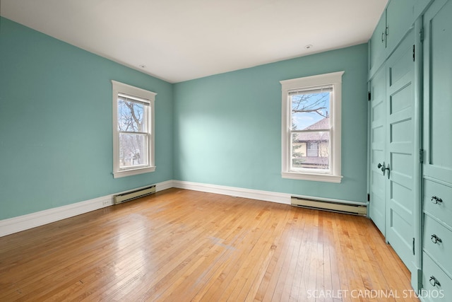 unfurnished room featuring a wealth of natural light, light wood-type flooring, and a baseboard heating unit