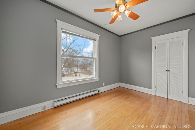 unfurnished bedroom featuring a baseboard radiator, wood-type flooring, ceiling fan, crown molding, and a closet