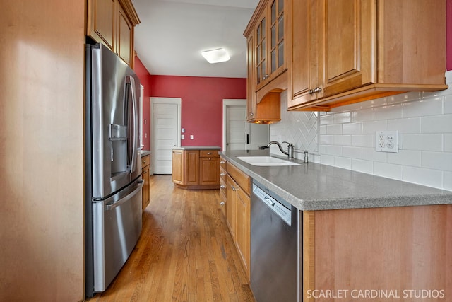 kitchen with appliances with stainless steel finishes, sink, backsplash, and light hardwood / wood-style flooring