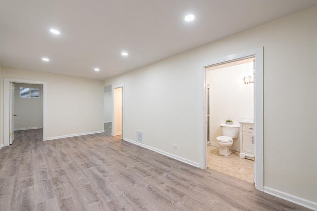 unfurnished bedroom featuring ensuite bath, a spacious closet, and light wood-type flooring