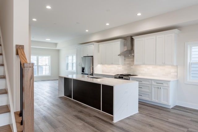 kitchen with wall chimney range hood, sink, light hardwood / wood-style flooring, white cabinetry, and stainless steel refrigerator with ice dispenser