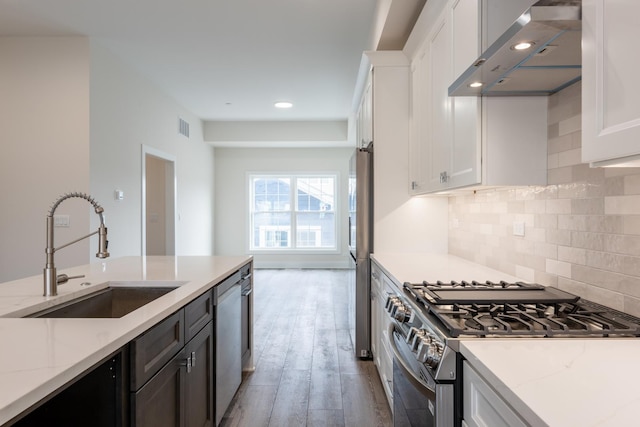 kitchen featuring wall chimney exhaust hood, sink, white cabinetry, appliances with stainless steel finishes, and light stone countertops