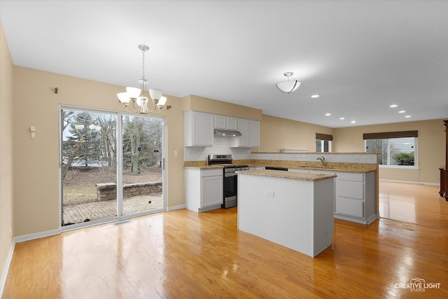 kitchen featuring under cabinet range hood, backsplash, a center island, light wood finished floors, and stainless steel range with gas stovetop