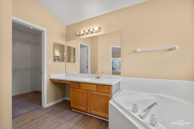 full bathroom featuring vanity, wood finished floors, baseboards, a walk in closet, and a garden tub