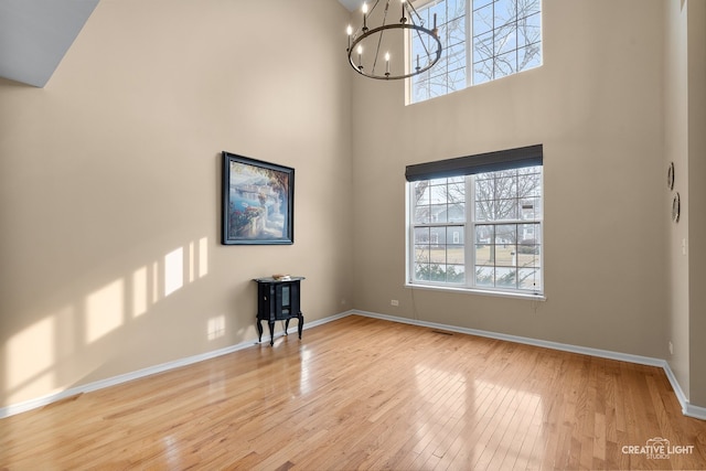 unfurnished room featuring baseboards, wood finished floors, a healthy amount of sunlight, and a chandelier