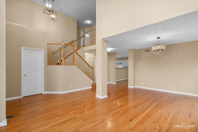 unfurnished living room featuring visible vents, stairway, a high ceiling, light wood-style floors, and an inviting chandelier