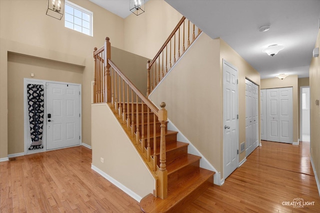 staircase featuring baseboards, a high ceiling, an inviting chandelier, and wood finished floors