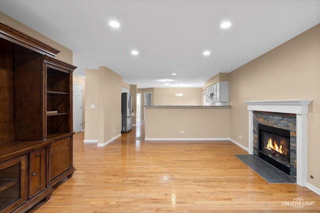 unfurnished living room with recessed lighting, a stone fireplace, an inviting chandelier, light wood finished floors, and baseboards