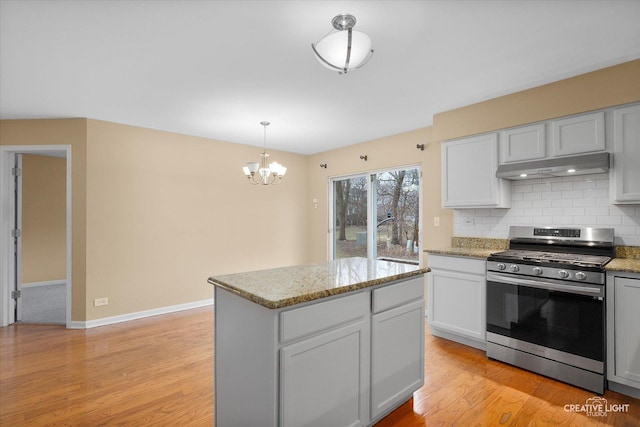 kitchen featuring backsplash, under cabinet range hood, gas range, light stone counters, and light wood-style floors