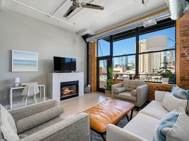 living room with a tile fireplace, a towering ceiling, brick wall, ceiling fan, and wood finished floors