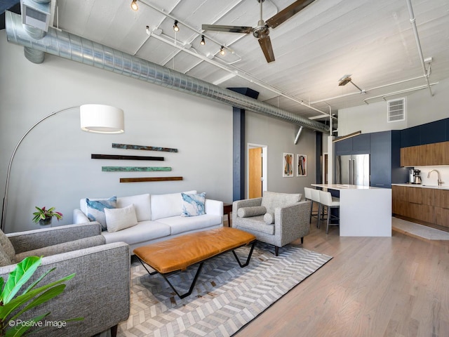 living room featuring visible vents, a ceiling fan, a towering ceiling, rail lighting, and light wood-style floors