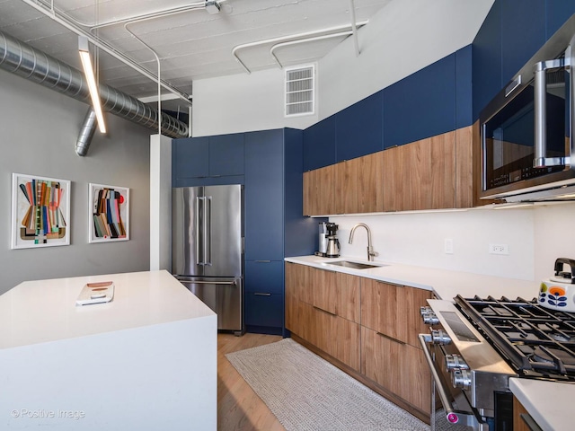 kitchen featuring blue cabinets, a sink, light countertops, appliances with stainless steel finishes, and modern cabinets