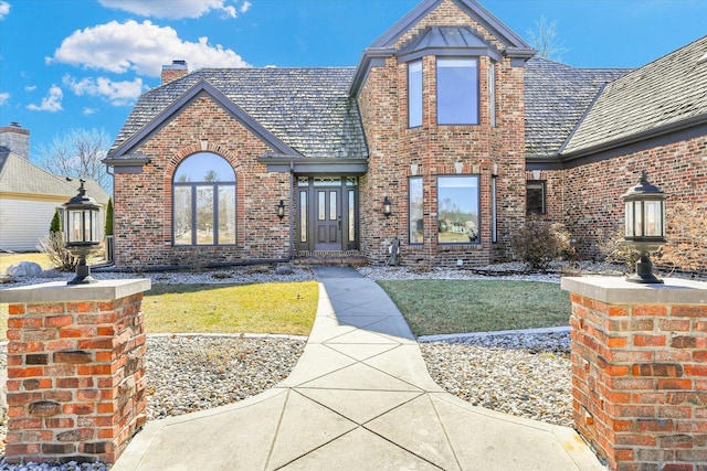 view of front facade with a front lawn, brick siding, and a chimney