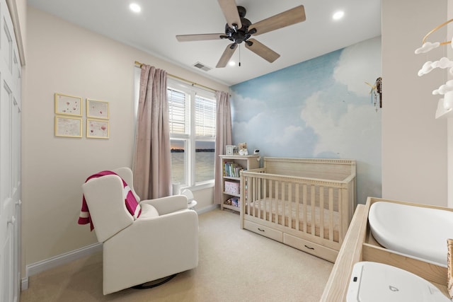 bedroom featuring light carpet, a crib, and ceiling fan