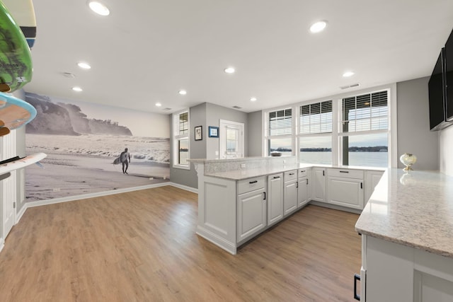 kitchen featuring light stone countertops, white cabinets, light wood-type flooring, and kitchen peninsula