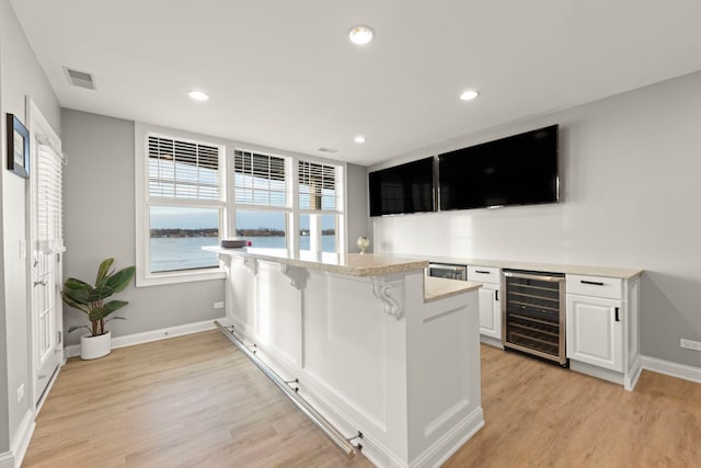 kitchen featuring wine cooler, white cabinetry, light wood-type flooring, a kitchen breakfast bar, and kitchen peninsula