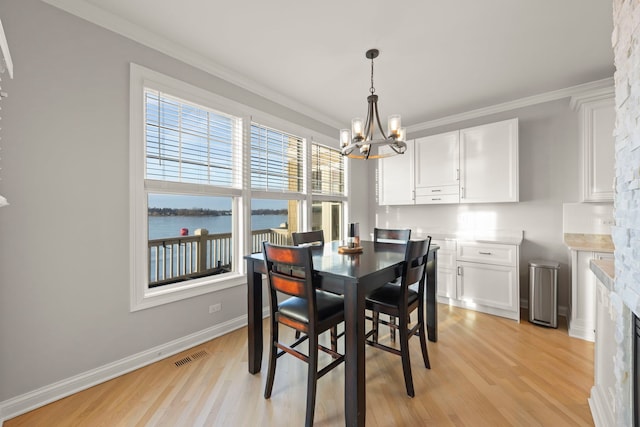 dining space featuring a fireplace, a chandelier, ornamental molding, a water view, and light hardwood / wood-style flooring