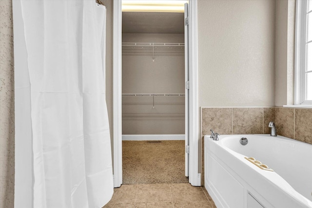 bathroom featuring tile patterned flooring, a spacious closet, and a bath