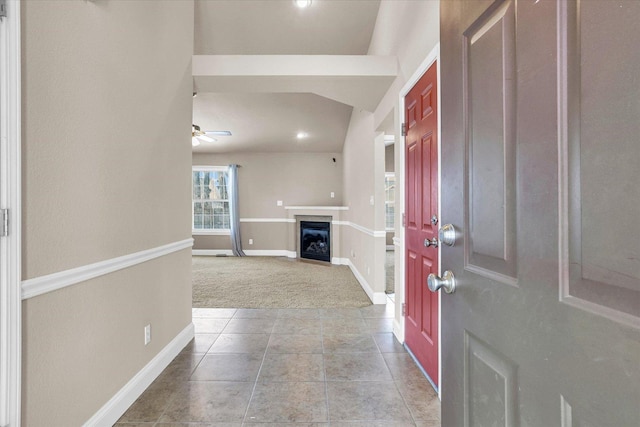 carpeted foyer with a ceiling fan, a glass covered fireplace, baseboards, and tile patterned floors