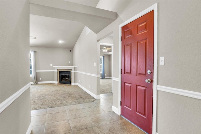 foyer with light tile patterned flooring, light carpet, a ceiling fan, baseboards, and a glass covered fireplace