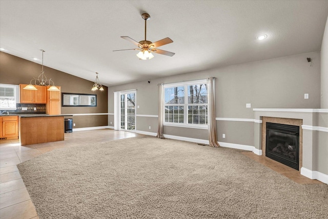 unfurnished living room with light tile patterned floors, lofted ceiling, a glass covered fireplace, baseboards, and ceiling fan with notable chandelier