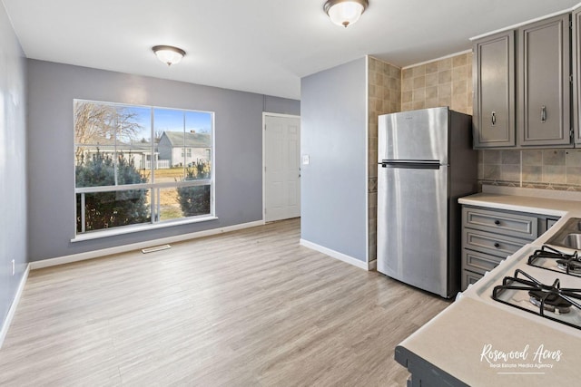 kitchen with gray cabinetry, backsplash, stainless steel refrigerator, and light hardwood / wood-style floors