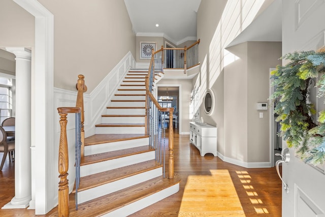 foyer entrance featuring crown molding, a towering ceiling, wood-type flooring, and decorative columns